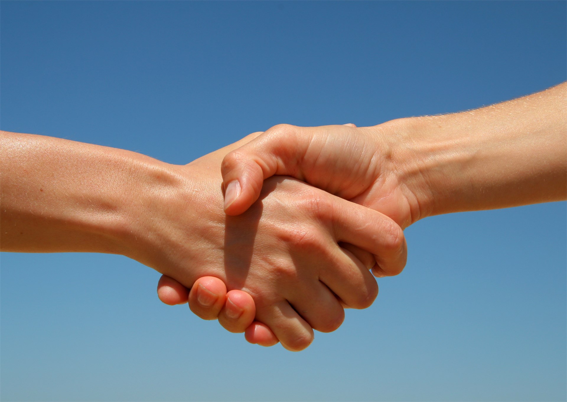 Zu sehen sind zwei Hände die ineinander verschränkt sind. Das Bild wurde von unten aufgenommen, sodass die Hände vor dem blauen Himmel zu sehen sind. 